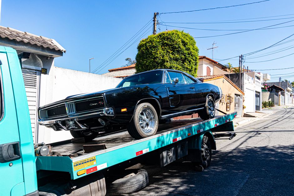 A black vintage muscle car is transported on a tow truck in a residential street during a sunny day.